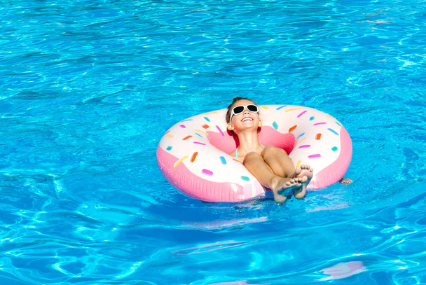 Cute smiling little girl in swimming pool with rubber ring. Child having fun on vacation in summertime - Foto, immagini