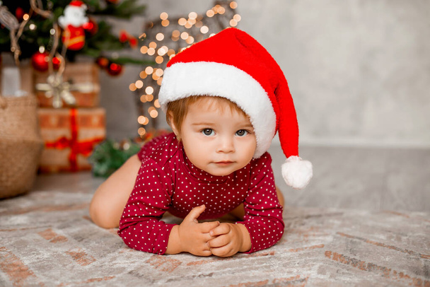 Симпатичный малыш Санта сидит дома возле елки с подарками - Фото, изображение