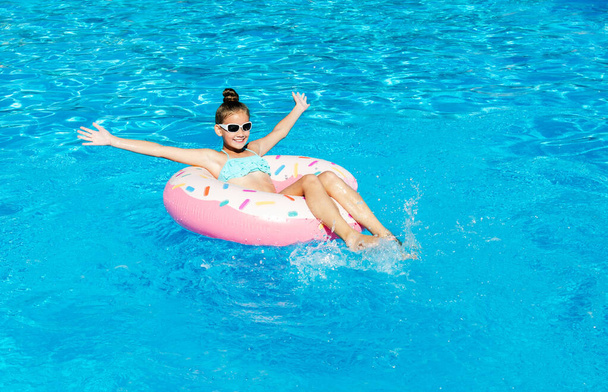 Милая улыбающаяся маленькая девочка в бассейне с резиновым кольцом. Ребенок веселится в отпуске летом - Фото, изображение