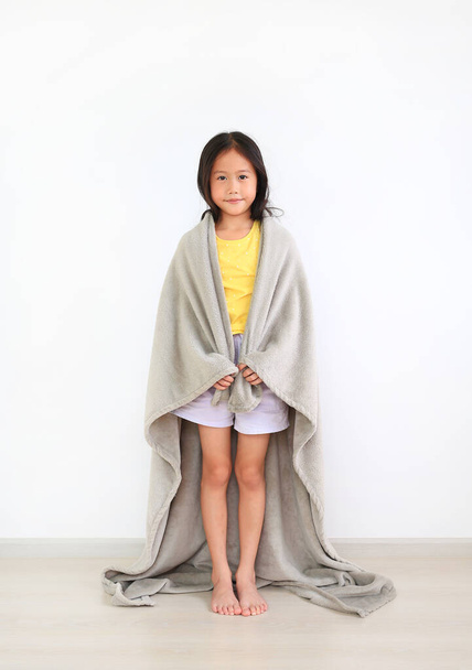 Asian little kid girl standing covered shoulder with soft gray blanket indoor. Winter season concept - Фото, изображение
