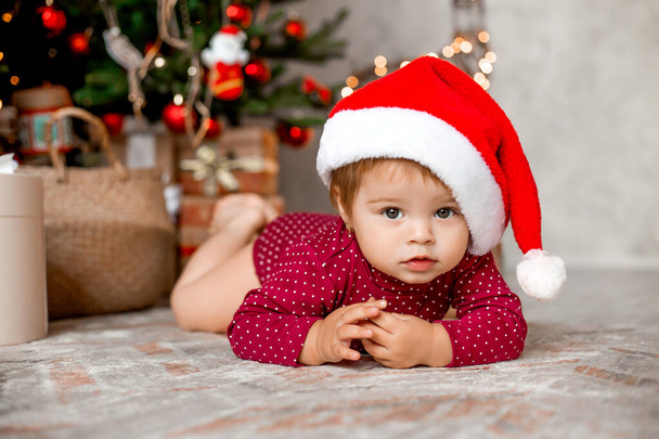 Lindo bebé Santa se sienta en casa cerca del árbol de Navidad con regalos - Foto, imagen