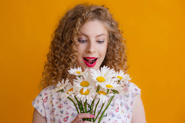 a curly woman holding a bouquet of daisies on a orange background  - Fotografie, Obrázek