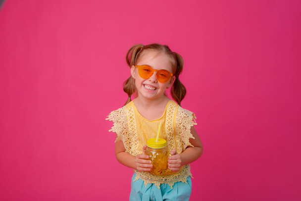 retrato de una niña rubia en gafas de sol en rosa con un frasco de vidrio de cóctel refrescante. - Foto, Imagen