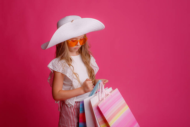 Bir sürü alışveriş çantası, güneş gözlüğü ve şapka takan şık küçük bir kız.   - Fotoğraf, Görsel