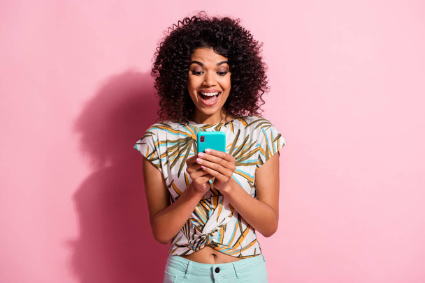 Photo portrait of excited woman with open mouth holding phone in two hands isolated on pastel pink colored background - Photo, Image