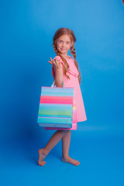 A girl with a lot of shopping bags posing on a blue background - Fotó, kép
