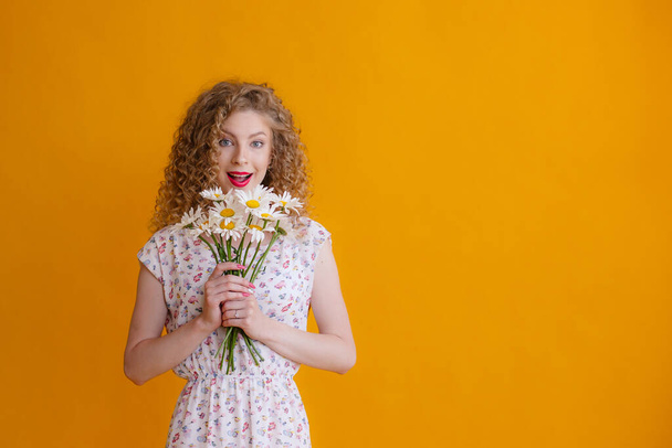 a curly woman holding a bouquet of daisies on a orange background  - Фото, зображення
