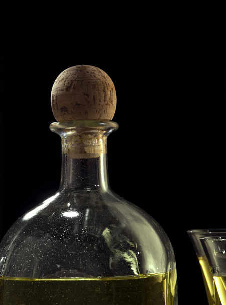fragmento vista de botella de tequila anejo y vasos sobre fondo negro - Foto, Imagen