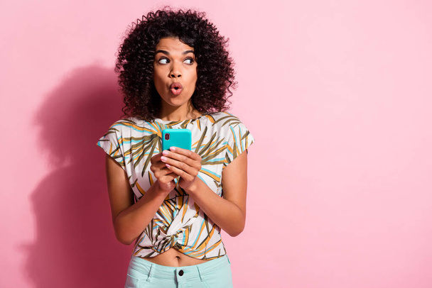 Photo portrait of shocked woman holding cyan phone in two hands isolated on pastel pink colored background with blank space - 写真・画像