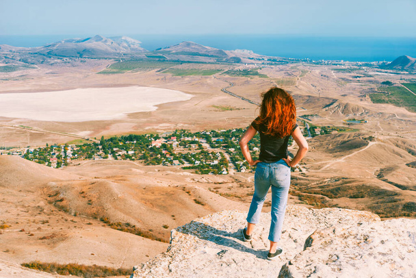 Uma jovem mulher bonita com cabelos longos e jeans em uma rocha no vale de Koktebel, na Crimeia. A paisagem do deserto montanhoso arenoso. - Foto, Imagem