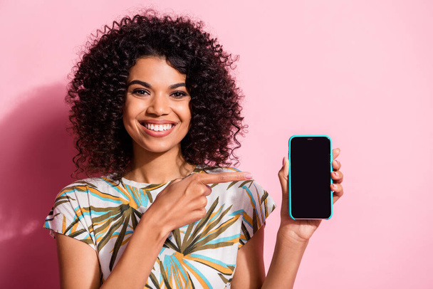 Photo portrait of woman pointing finger at phone in hand with blank space isolated on pastel pink colored background - Fotoğraf, Görsel