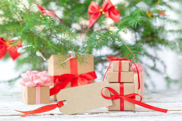 Many Christmas gift boxes with red ribbon with empty tag under the christmas tree. Natural and reusable decor. - Photo, Image
