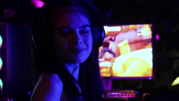 Молодая красивая женщина сидит в кресле в игорном клубе и играет в шутер - улыбаясь в камеру - Кадры, видео