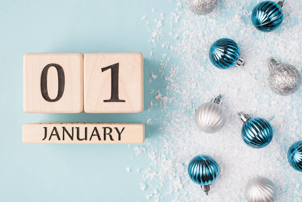 Новогодняя концепция. Сверху над головой фотография деревянных кубиков, изображающих первый день Нового года на голубом фоне со снегом и безделушками - Фото, изображение