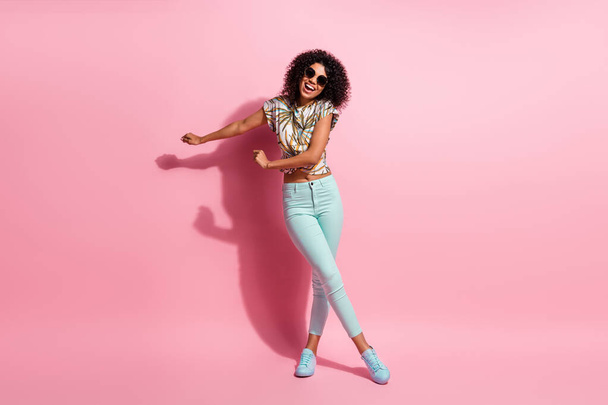 Full length body size photo of careless happy black skinned woman dancing on floor in casual outfit sunglass isolated on pastel pink color background - Foto, afbeelding