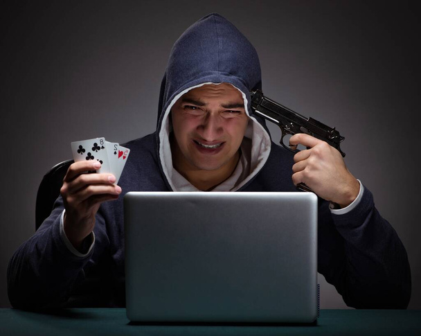 Νεαρός άνδρας με κουκούλα κάθεται μπροστά από έναν φορητό υπολογιστή - Φωτογραφία, εικόνα