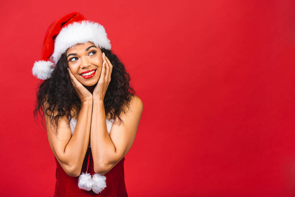 Hermosa sonriente mujer negra afroamericana feliz en ropa de Santa Claus aislada sobre fondo rojo. Año nuevo y el concepto de Navidad.  - Foto, Imagen