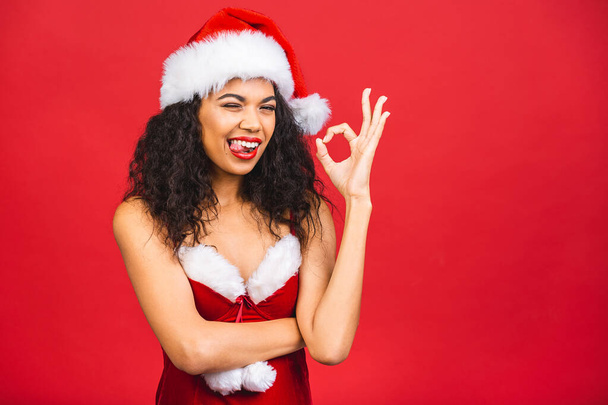 Hermosa sonriente mujer negra afroamericana feliz en ropa de Santa Claus aislada sobre fondo rojo. Año nuevo y el concepto de Navidad.  - Foto, imagen