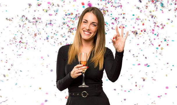 Vrouw met champagne viert nieuwjaar met een ok bord met vingers met confetti - Foto, afbeelding