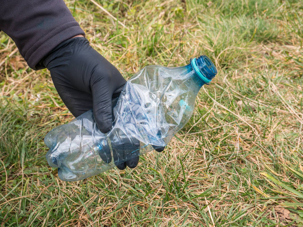Чоловік в одноразових чорних гумових рукавичках, що збирають пластикові пляшки (PET) відходи
. - Фото, зображення