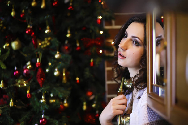 暖かいパジャマを着た若い魅力的な女の子と新年の木の近くにベッドスプレッド。クリスマスの雰囲気. - 写真・画像