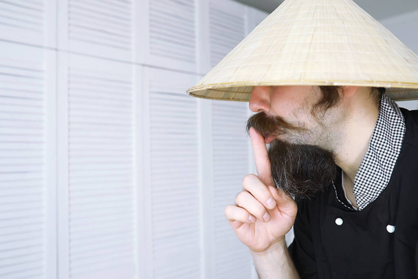 Una parodia hilarante de un hombre asiático con sombrero vietnamita con barba. Retrato. Chef asiático cafetería. - Foto, Imagen