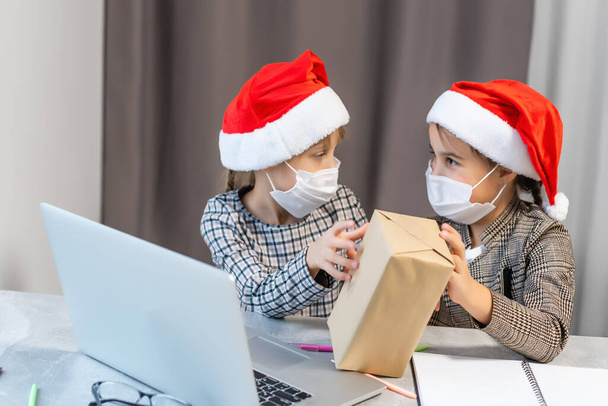 Natale online. Due ragazzine mascherate guardano un portatile. Concetto periodo natalizio - Foto, immagini