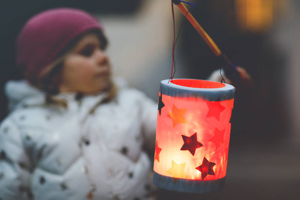 Close-up of little kid girl holding selfmade lanterns with candle for St. Martin procession. Healthy toddler child happy about children and family parade in kindergarten. German tradition Martinsumzug - Photo, Image