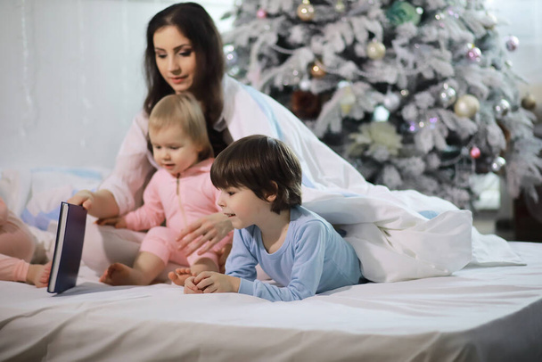 Eine Familie mit Kindern vergnügt sich während der Weihnachtsfeiertage auf dem Bett unter der Decke. - Foto, Bild
