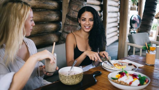 Smiling caucasian hipster girl enjoying delicious vegan food during dinner discussing ingredients and meals, positive women best friends having lunch together eating organic and healthy dishes - Photo, Image