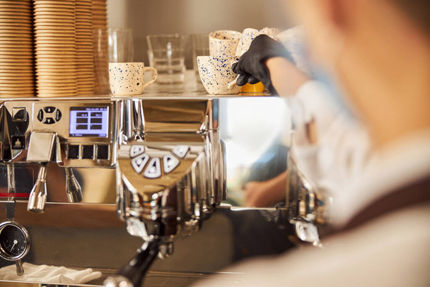 Vrouwelijke hand in rubberen handschoen neemt beker uit een kopje verwarmende lade in een cafe - Foto, afbeelding