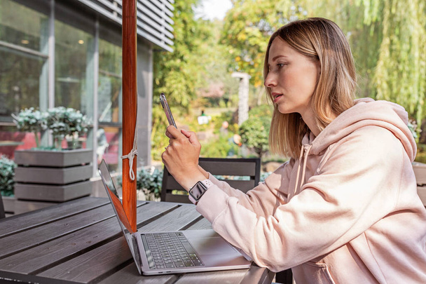 Young Caucasian business woman with blonde hair working on laptop in outdoor cafe. College student using technology , online education, freelance  - Foto, Bild