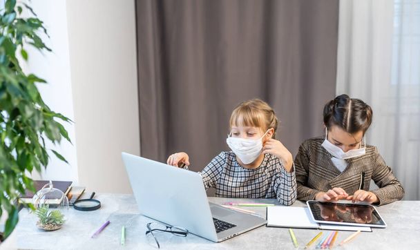 Mesafe öğrenme. Laptop 'ta Okul Kızları Maske Takıyor İnternette çalışıyor Evde masada oturuyor - Fotoğraf, Görsel