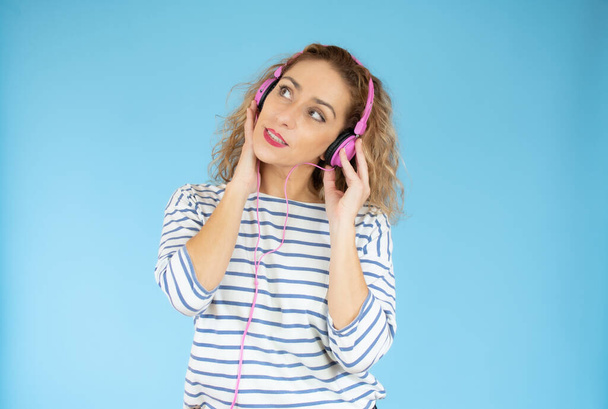 Schöne Frau mit Kopfhörer hört Musik auf blauem Hintergrund - Foto, Bild