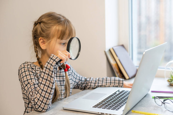 Pikkutyttö tekee kotiläksynsä kotona ja käyttää kannettavaa tietokonetta - Valokuva, kuva