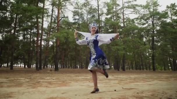 Красивая женщина в голубом русском традиционном народном костюме с платком танцует в лесу - Кадры, видео