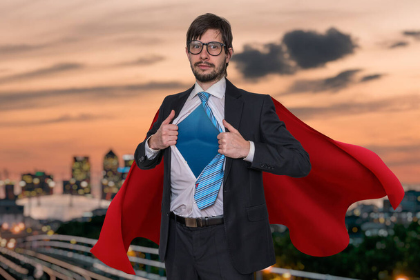 Businessman in suit as superhero is opening his shirt. City in background. - Foto, Imagen