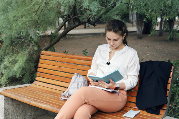 Jeune étudiante habillée dans un style d'affaires lit calmement dans la tablette tout en étant assis sur le banc du parc seul - Photo, image