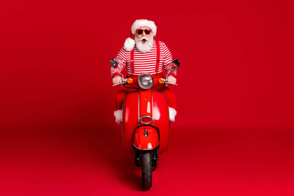 Full length photo of crazy retired old man moped enjoy ride empty windy highway open mouth wear santa x-mas costume suspenders sunglass boots striped shirt cap isolated red color background - Fotografie, Obrázek