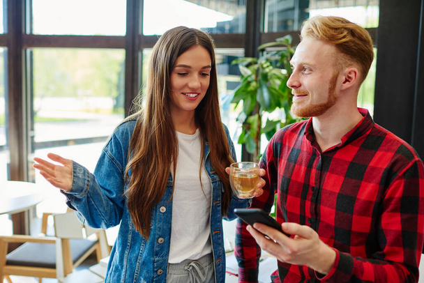 Happy Caucasian boyfriend and girlfriend discussing web publication during beverage refreshing in cafe, cheerful hipster guys 20s reading received email newsletter with positive content text - Foto, Bild