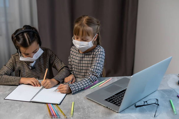Молодые школьницы в защитной маске смотрят онлайн-учебный класс. Coronavirus или Covid-19 Locdown education concept. - Фото, изображение
