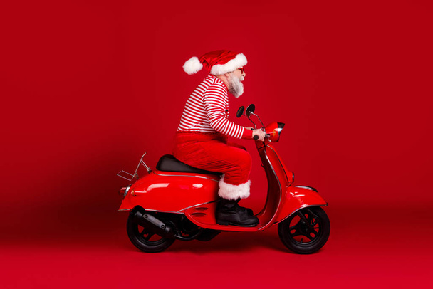 Full length body size profile side view of his he handsome bearded Santa father riding moped fast hurry delivering gift North Pole traveler isolated bright vivid shine vibrant red color background - Foto, immagini
