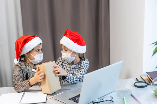 Navidad en línea. dos niñas con máscaras médicas están viendo un portátil. Concepto de Navidad - Foto, Imagen