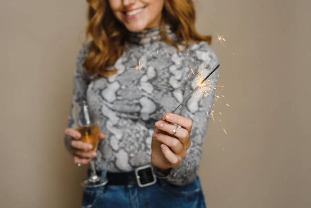 Młoda piękna kobieta ze szczerym uśmiechem spogląda w kamerę, pozując z palącymi się ogniami i pijąc szampana. Koncepcja świąt - Zdjęcie, obraz