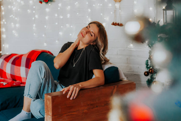 Young beautiful woman sitting on sofa in studio with Christmas decorations - Foto, Bild