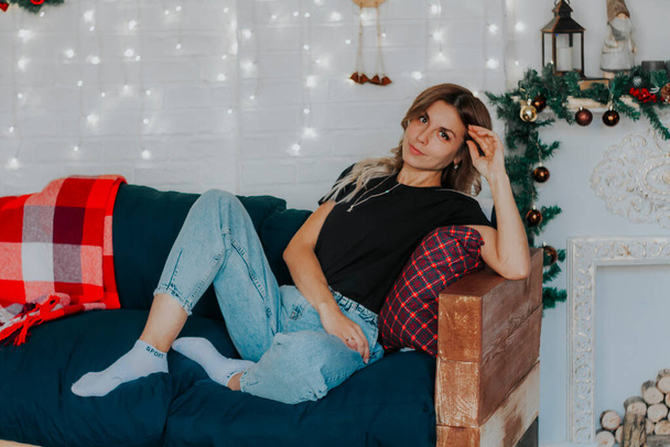 Young beautiful woman sitting on sofa in studio with Christmas decorations - Zdjęcie, obraz