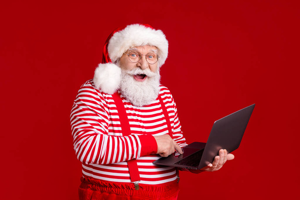 Πορτρέτο του ο όμορφος χαρούμενος χαρούμενος γενειοφόρος Άγιος Βασίλης κρατώντας στα χέρια χρησιμοποιώντας το φορητό υπολογιστή γράμμα e-mail παραγγελία σεζόν πώληση Βόρειο Πόλο απομονωμένο φωτεινό έντονο κόκκινο χρώμα φόντο - Φωτογραφία, εικόνα