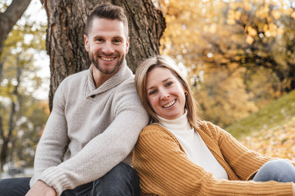 Loving couple in the autumn park sitting on the bottom of a tree - Foto, imagen