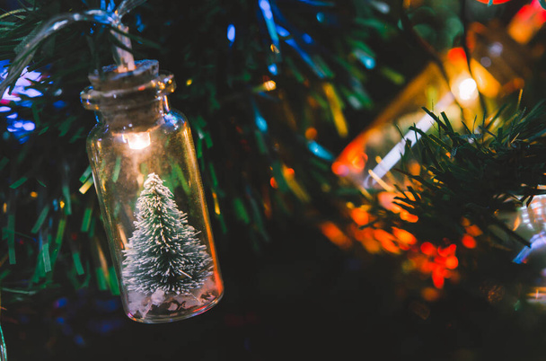 Christmas decoration. Hanging small Christmas tree in glass jar on pine branches christmas tree garland and ornaments over abstract bokeh - Foto, afbeelding