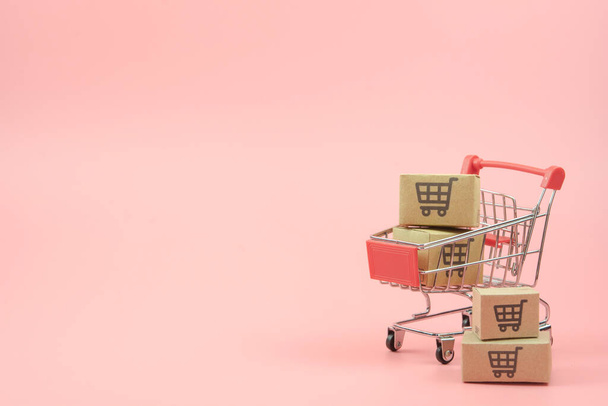 Winkelconcept - Doosjes of Papieren doosjes in rood winkelwagentje op roze achtergrond. online winkelen consumenten kunnen winkelen vanuit huis en bezorgservice. met kopieerspaak - Foto, afbeelding